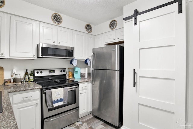 kitchen featuring stone countertops, a textured ceiling, stainless steel appliances, a barn door, and white cabinets