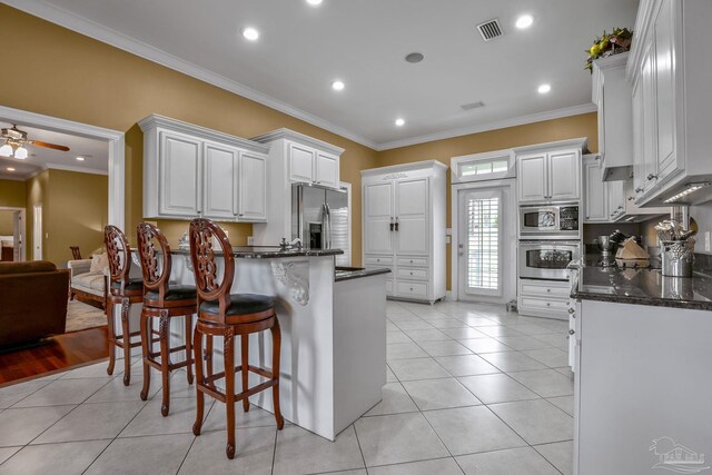 kitchen with light tile patterned floors, ceiling fan, white cabinetry, stainless steel appliances, and ornamental molding