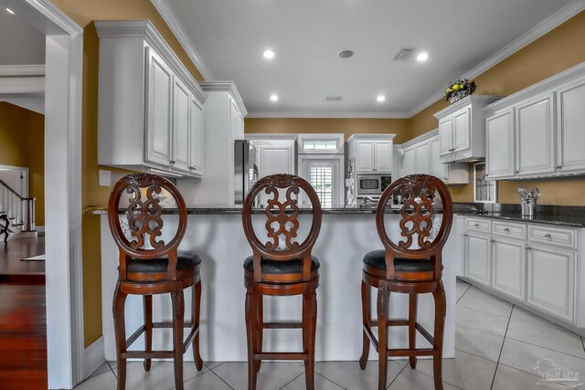 kitchen featuring dark stone countertops, white cabinets, a kitchen breakfast bar, stainless steel appliances, and crown molding