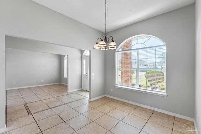 unfurnished room with a notable chandelier, a textured ceiling, baseboards, and light tile patterned floors