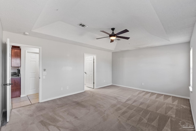 unfurnished bedroom with light carpet, baseboards, visible vents, a raised ceiling, and a textured ceiling