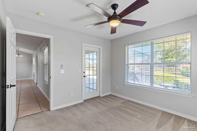 empty room with a wealth of natural light, light colored carpet, a textured ceiling, and baseboards