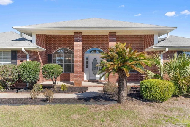 view of front of house featuring a front yard, brick siding, and roof with shingles