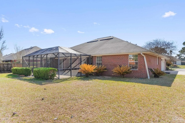 back of property with glass enclosure, a lawn, and brick siding