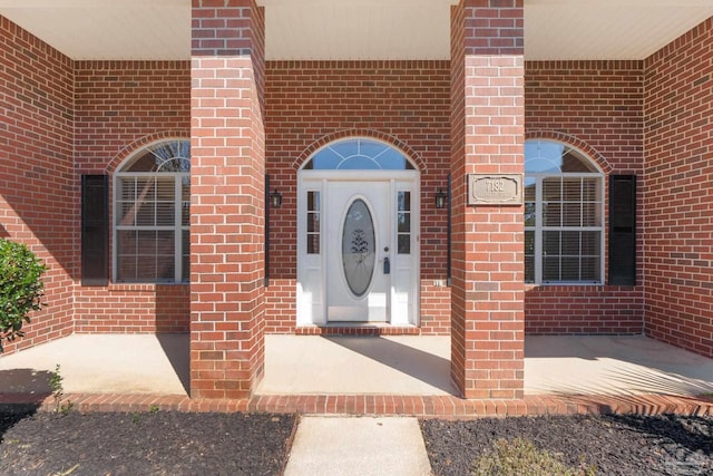 doorway to property featuring a porch and brick siding