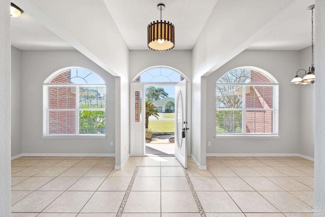 foyer with a notable chandelier, baseboards, a textured ceiling, and light tile patterned flooring