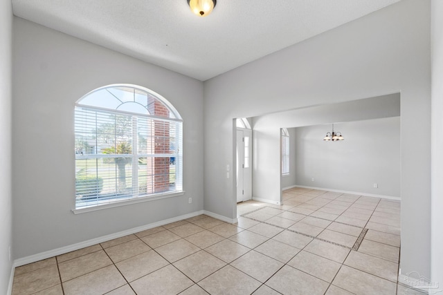 spare room featuring light tile patterned floors, a textured ceiling, baseboards, and a notable chandelier