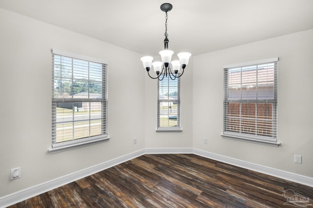 spare room with a chandelier, plenty of natural light, dark wood finished floors, and baseboards