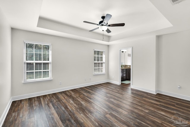 unfurnished room with dark wood-style floors, a raised ceiling, a wealth of natural light, and baseboards