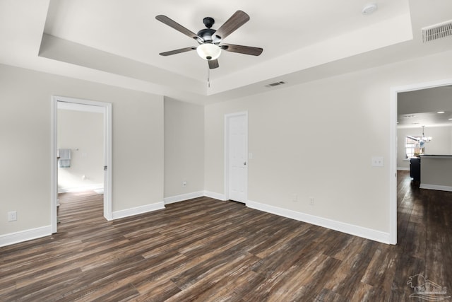 unfurnished bedroom featuring dark wood-style floors, a tray ceiling, visible vents, and baseboards