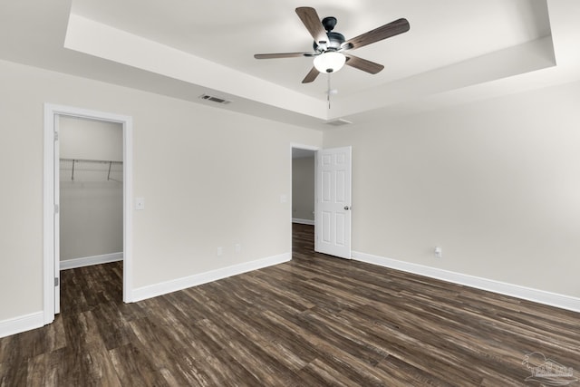 unfurnished bedroom featuring dark wood-type flooring, a raised ceiling, visible vents, and baseboards