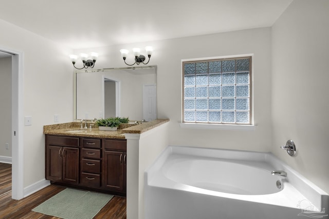 bathroom with double vanity, a sink, wood finished floors, baseboards, and a bath