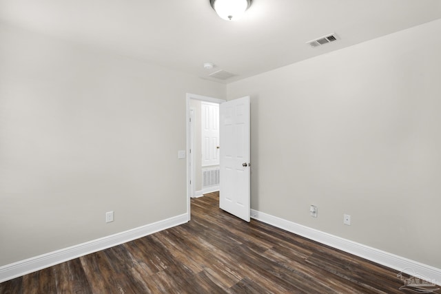 empty room with dark wood-style floors, visible vents, and baseboards