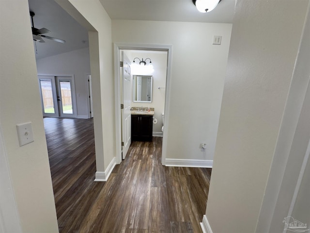 corridor featuring vaulted ceiling, dark wood-type flooring, a sink, and baseboards