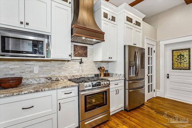 kitchen with appliances with stainless steel finishes, white cabinetry, tasteful backsplash, light stone countertops, and custom range hood