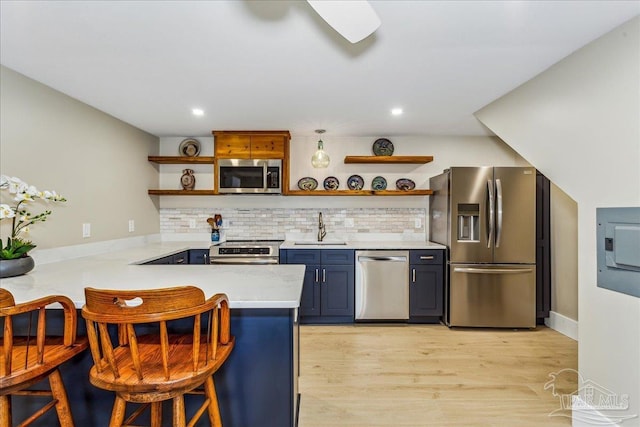 kitchen featuring blue cabinets, a breakfast bar, appliances with stainless steel finishes, kitchen peninsula, and backsplash