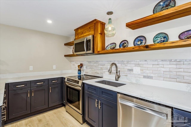 kitchen with sink, decorative light fixtures, light hardwood / wood-style flooring, appliances with stainless steel finishes, and light stone countertops