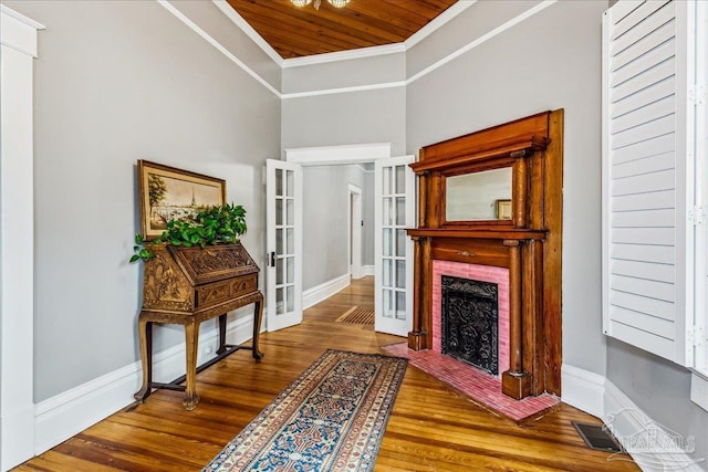 sitting room with french doors, wood ceiling, wood-type flooring, a brick fireplace, and ornamental molding