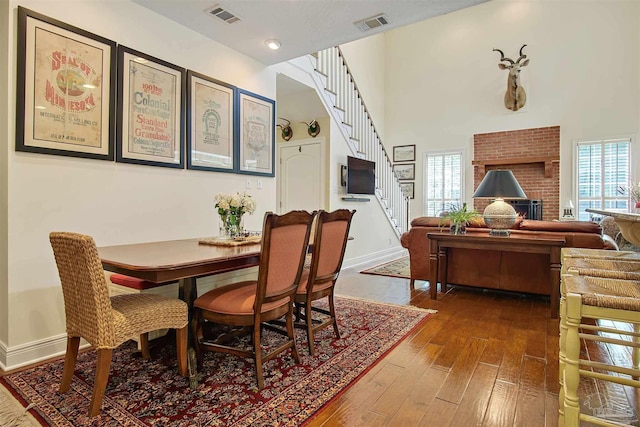 607 Goodwill Cir, Silas, AL 36919 - dining area featuring dark wood-style floors, stairs, a high ceiling, baseboards, and a brick fireplace