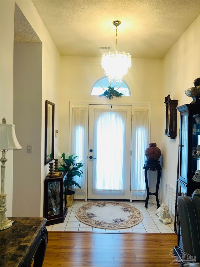 entryway featuring an inviting chandelier, a textured ceiling, and light wood-type flooring