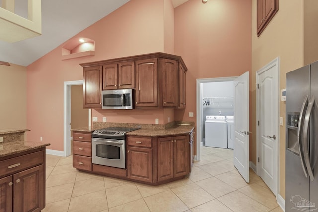 kitchen with stainless steel appliances, dark stone counters, washing machine and clothes dryer, high vaulted ceiling, and light tile patterned floors