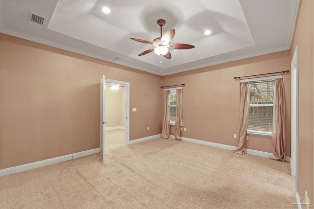 empty room featuring crown molding, a healthy amount of sunlight, a tray ceiling, and light colored carpet