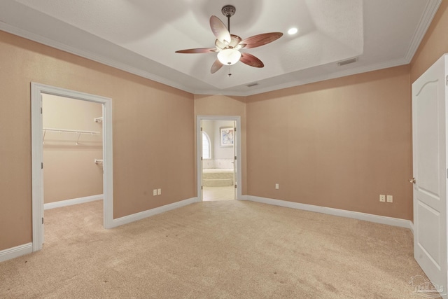 unfurnished bedroom with ceiling fan, a raised ceiling, crown molding, a walk in closet, and a closet