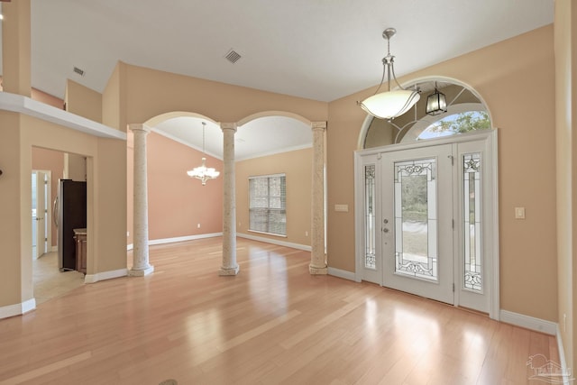 foyer with light hardwood / wood-style floors, crown molding, ornate columns, and a chandelier