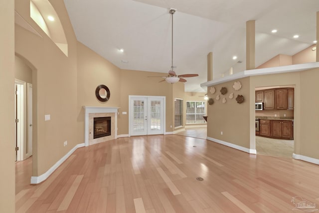 unfurnished living room with high vaulted ceiling, ceiling fan, a tiled fireplace, and light hardwood / wood-style floors