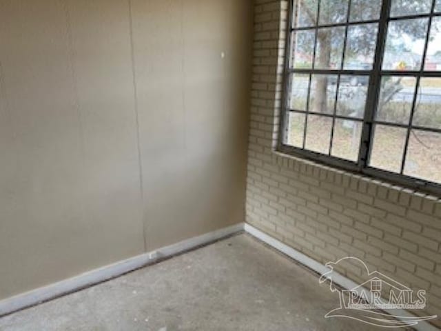 unfurnished room featuring brick wall and baseboards