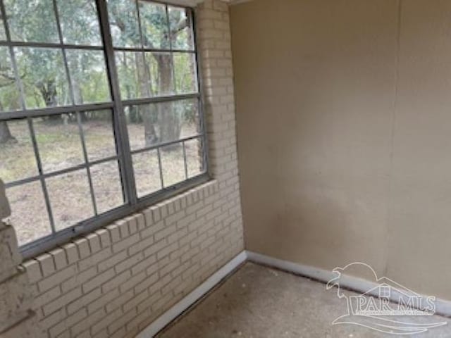 spare room featuring baseboards, brick wall, and plenty of natural light