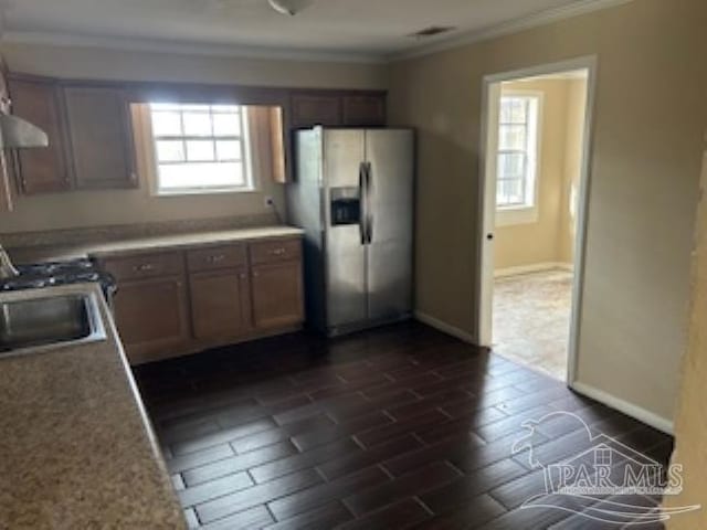 kitchen with stainless steel refrigerator with ice dispenser, exhaust hood, crown molding, and baseboards