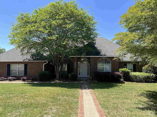 view of front facade with brick siding, a shingled roof, and a front lawn