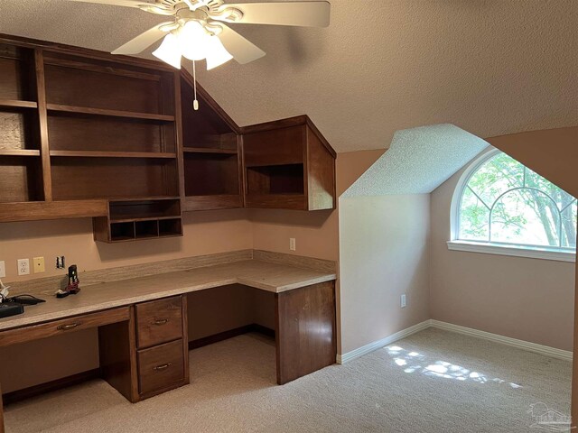 unfurnished office featuring a ceiling fan, a textured ceiling, built in desk, baseboards, and lofted ceiling