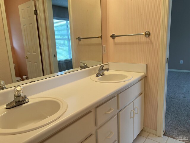bathroom with baseboards, double vanity, toilet, and a sink