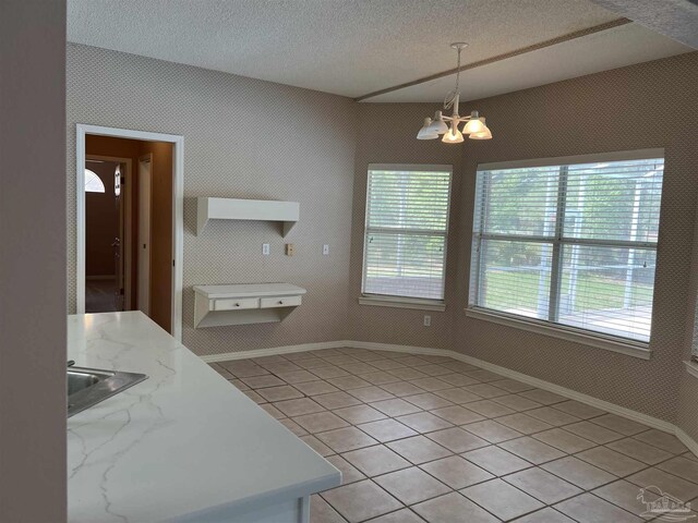 unfurnished dining area with a textured ceiling, a notable chandelier, a healthy amount of sunlight, and light tile patterned floors