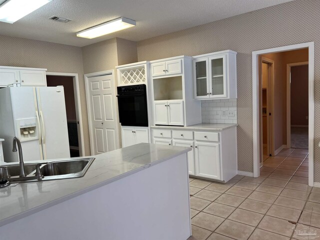 kitchen featuring a sink, white refrigerator with ice dispenser, black oven, white cabinetry, and light tile patterned floors