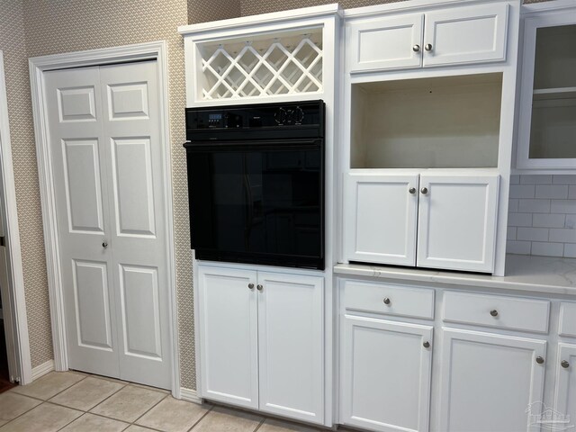 interior details featuring white cabinets, oven, light countertops, wallpapered walls, and backsplash
