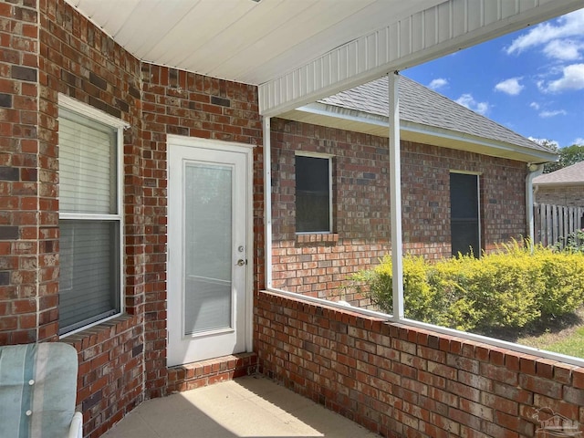 view of exterior entry featuring a shingled roof and brick siding