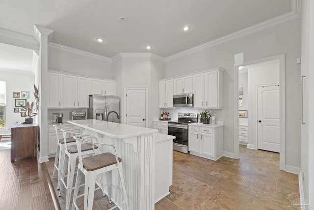 kitchen featuring a kitchen breakfast bar, white cabinetry, a kitchen island with sink, and appliances with stainless steel finishes