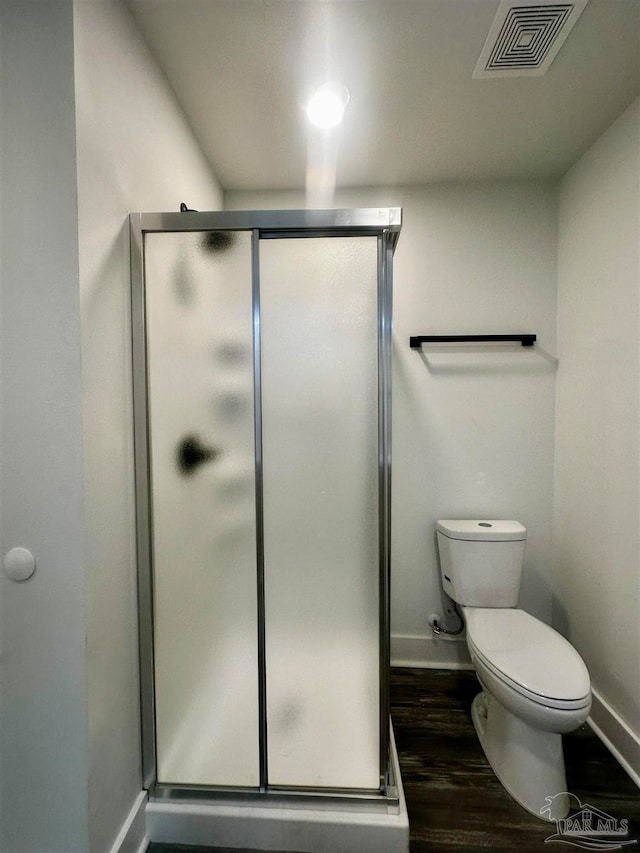 bathroom with an enclosed shower, toilet, and wood-type flooring