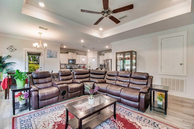 living area with a raised ceiling, visible vents, ceiling fan with notable chandelier, and light wood-style floors