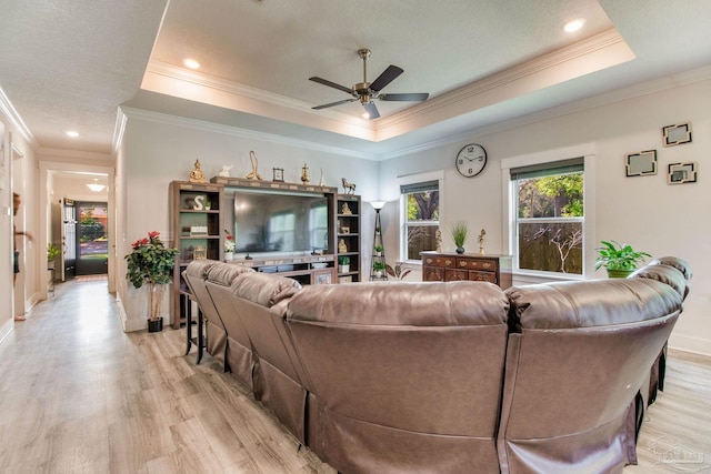 living room featuring a ceiling fan, crown molding, light wood finished floors, and a tray ceiling