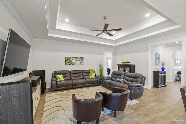 living room with crown molding, a tray ceiling, ceiling fan, and light wood-type flooring