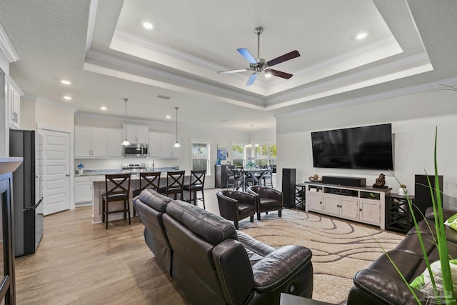 living room with ceiling fan, ornamental molding, a tray ceiling, and light hardwood / wood-style flooring