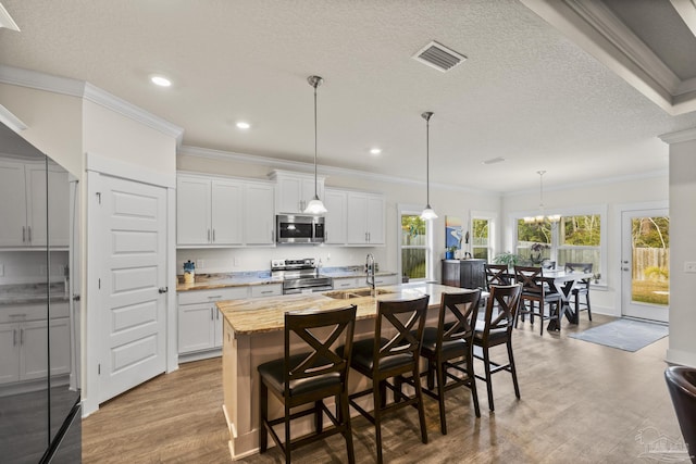 kitchen featuring sink, appliances with stainless steel finishes, white cabinetry, a kitchen breakfast bar, and a center island with sink