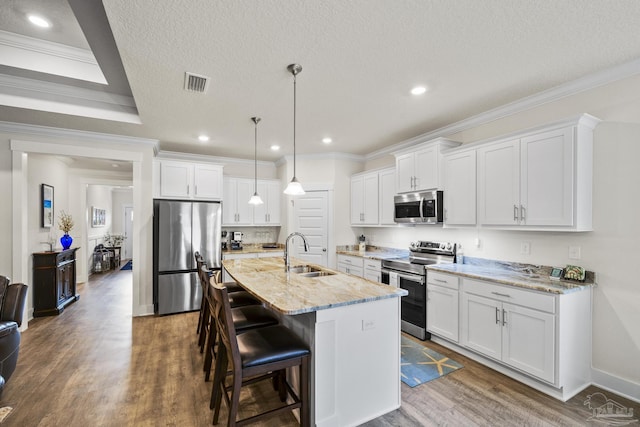 kitchen featuring sink, hanging light fixtures, stainless steel appliances, white cabinets, and a center island with sink