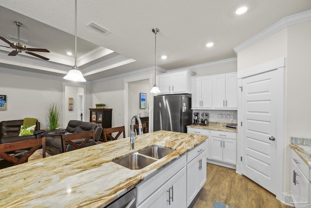 kitchen with stainless steel refrigerator, decorative light fixtures, white cabinetry, sink, and a raised ceiling