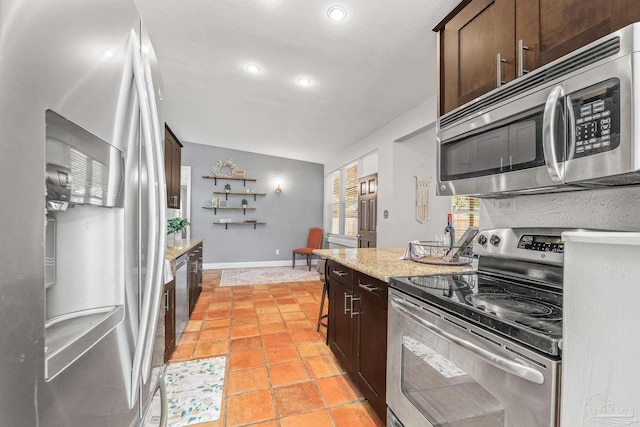 kitchen featuring vaulted ceiling, light tile patterned floors, light stone counters, dark brown cabinetry, and stainless steel appliances