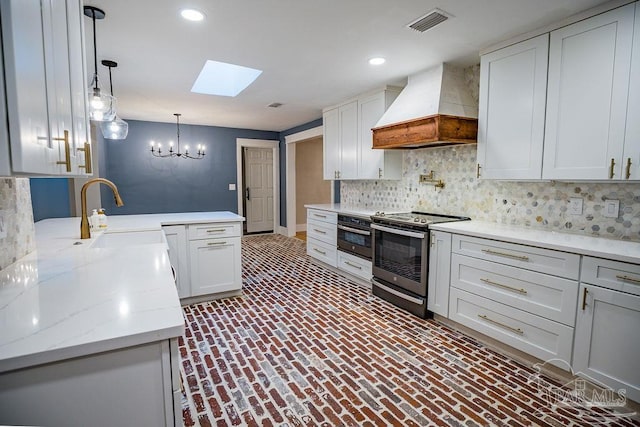 kitchen featuring stainless steel appliances, sink, premium range hood, a skylight, and pendant lighting